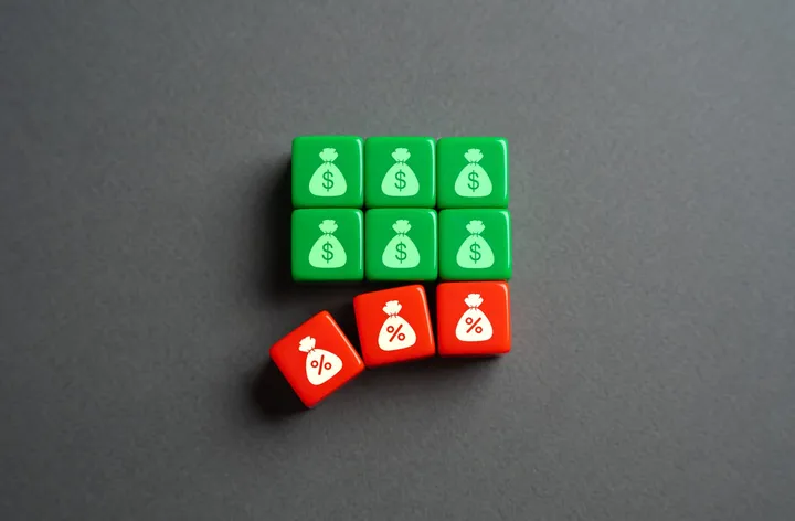 Green money-symbol blocks and red interest-symbol blocks on a grey surface